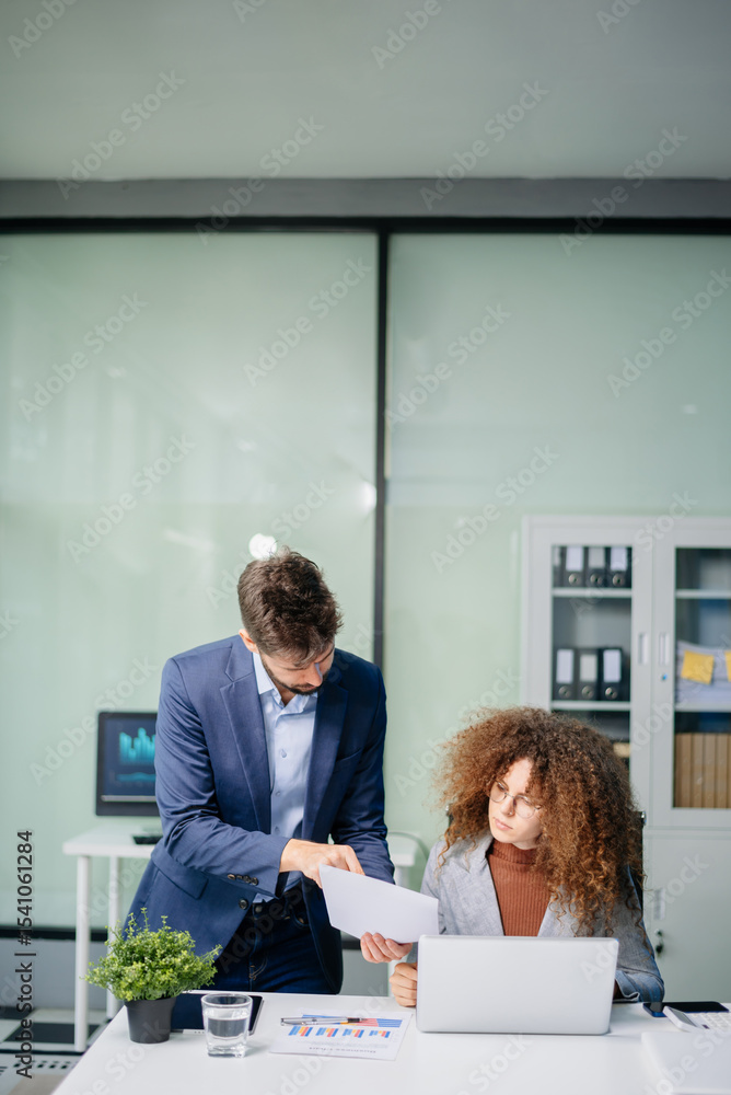 Obraz premium Business professionals discussing strategy with documents and laptop in a bright modern office. Corporate collaboration