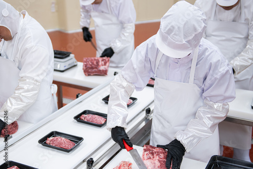 Meat factory workers in white coats and gloves preparing meat for processing.