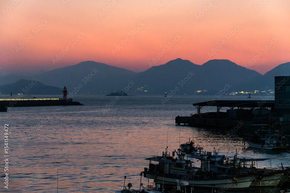 Obraz premium light house, and fishing boats moored at the harbor during sunset