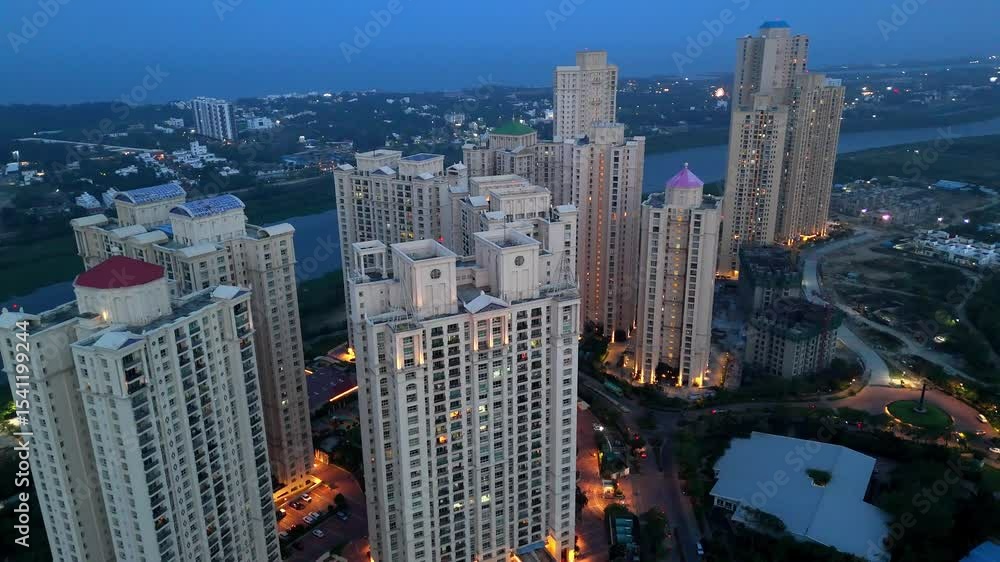 High-angle aerial view of a modern residential township at dusk Hiranandani Parks India. The scene is dominated by numerous high-rise apartment towers with illuminated windows High-angle aerial view of a modern residential township at dusk Hiranandani Parks India. The scene is dominated by numerous high-rise apartment towers with illuminated windows