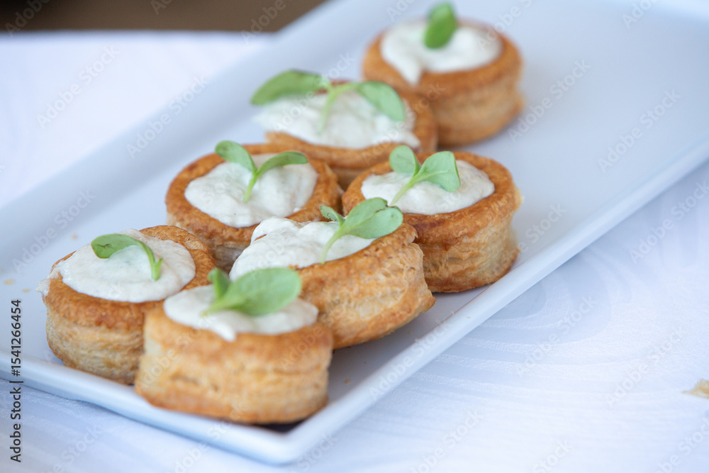 Delicious vol-au-vents with cream cheese topping and herbs garnishing a white rectangular plate Delicious vol-au-vents with cream cheese topping and herbs garnishing a white rectangular plate