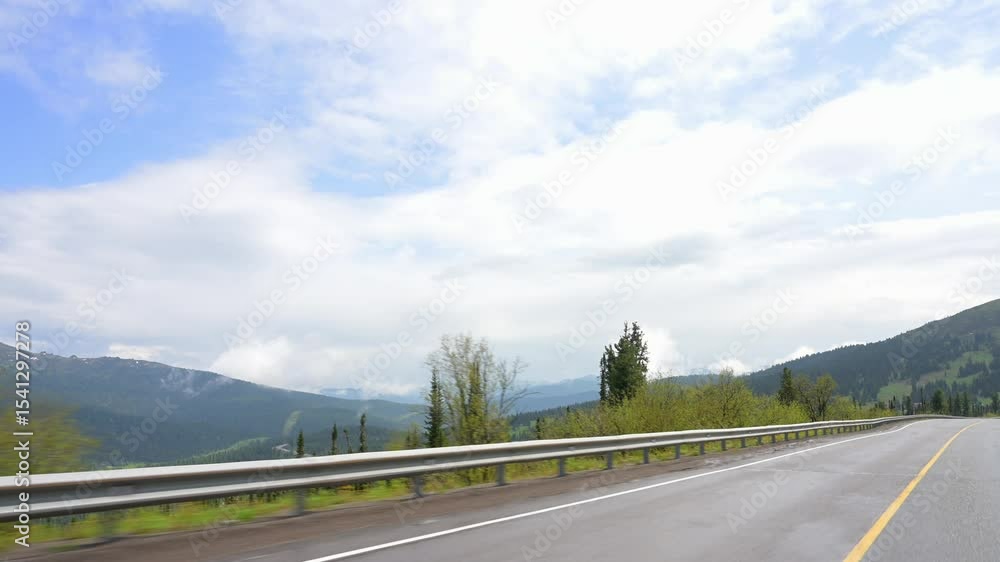 POV driving through forested mountain road on sunny summer day. View from inside moving car, with green trees, clear blue sky, and distant snow-capped peaks. Scenic peaceful travel footage in Siberian POV driving through forested mountain road on sunny summer day. View from inside moving car, with green trees, clear blue sky, and distant snow-capped peaks. Scenic peaceful travel footage in Siberian