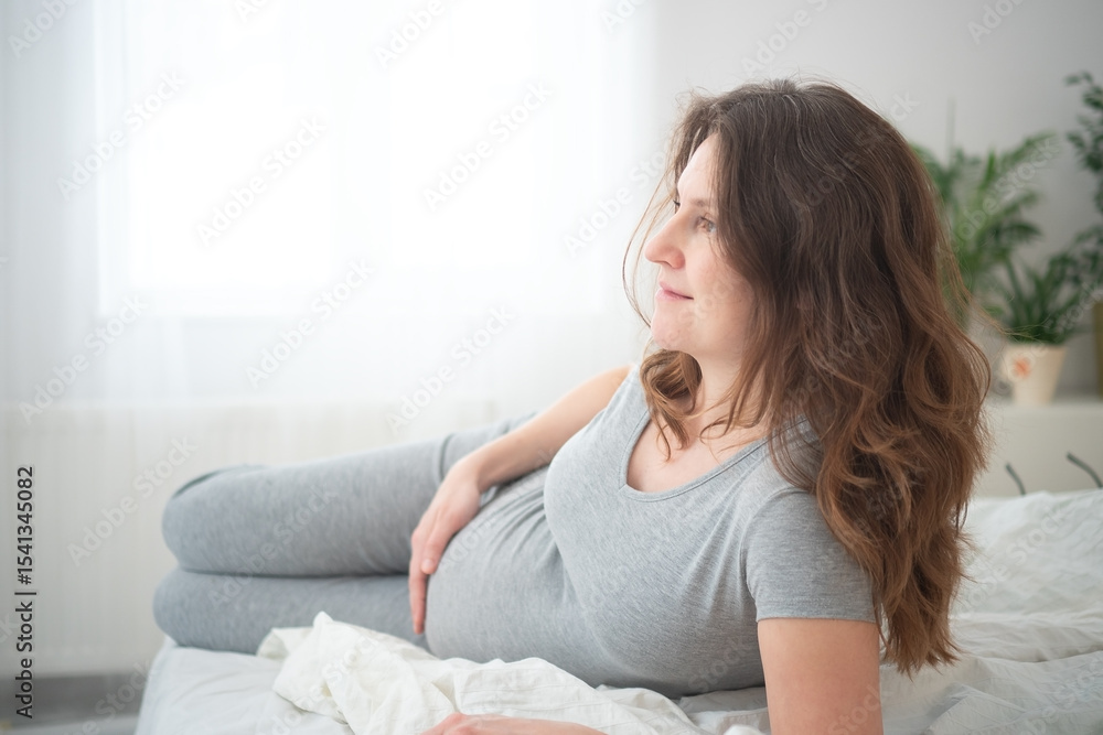 Glowing pregnant woman sitting comfortably on bed while tenderly touching her belly. Heartwarming scene of maternal bliss and joyful expectation. Glowing pregnant woman sitting comfortably on bed while tenderly touching her belly. Heartwarming scene of maternal bliss and joyful expectation.