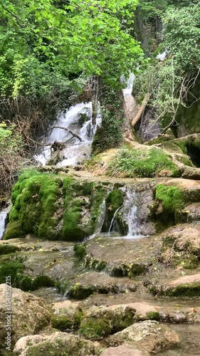 A waterfall with moss growing on the rocks. The water is clear and the moss is green. The scene is peaceful and serene