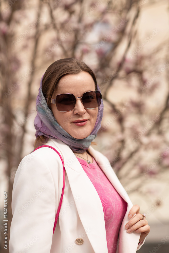 Woman Sunglasses Scarf: Trendy woman poses by blossoms wearing headscarf, sunglasses in daylight. Woman Sunglasses Scarf: Trendy woman poses by blossoms wearing headscarf, sunglasses in daylight.
