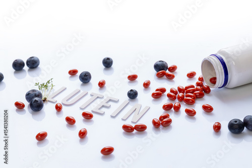 lutein dietary supplement capsules spilled from white bottle with fresh blueberries green leaves and text lutein on clean white background concept of eye health antioxidant natural vitamin nutrition