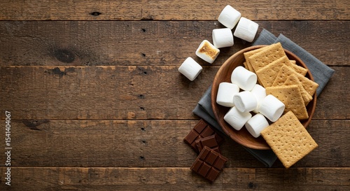 A rustic wooden table displays ingredients for making s'mores, a sweet treat.