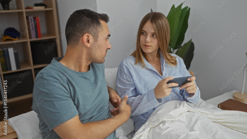 Obraz premium Couple in bedroom, woman using phone on bed, man engaging, modern home environment, young adults interacting, cozy interior, morning routine dialogue