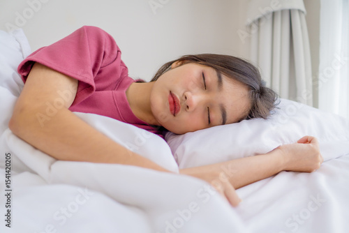 Beautiful Asian woman sleeping peacefully in cozy bedroom during morning. Young female enjoying sweet dreams and relaxing in bed, showing comfort, rest, and healthy sleep at home, wellness concept.