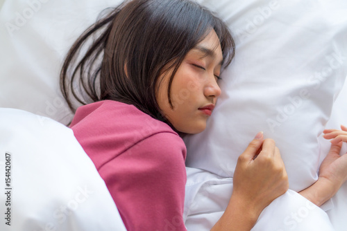 Beautiful Asian woman sleeping peacefully in cozy bedroom during morning. Young female enjoying sweet dreams and relaxing in bed, showing comfort, rest, and healthy sleep at home, wellness concept.