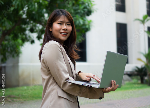 Portrait happy Asian businesswoman working on laptop in city. 