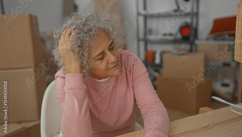 Photos Woman with grey hair sitting in a new home surrounded by cardboard boxes, reflecting in a modern living room