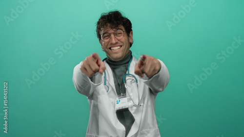 Foto Hispanic doctor with glasses and stethoscope pointing at camera against vibrant green background, smiling confidently