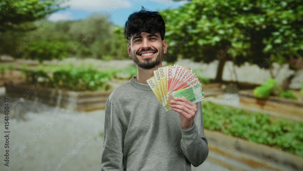 Fototapeta premium Man holding norwegian banknotes outdoors in a vibrant park setting, smiling confidently surrounded by lush greenery, showcasing currency in a bright natural environment.