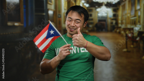 Tableau sur toile Young man holding puerto rican flag in museum setting, wearing volunteer shirt, smiling and giving thumbs up indoor