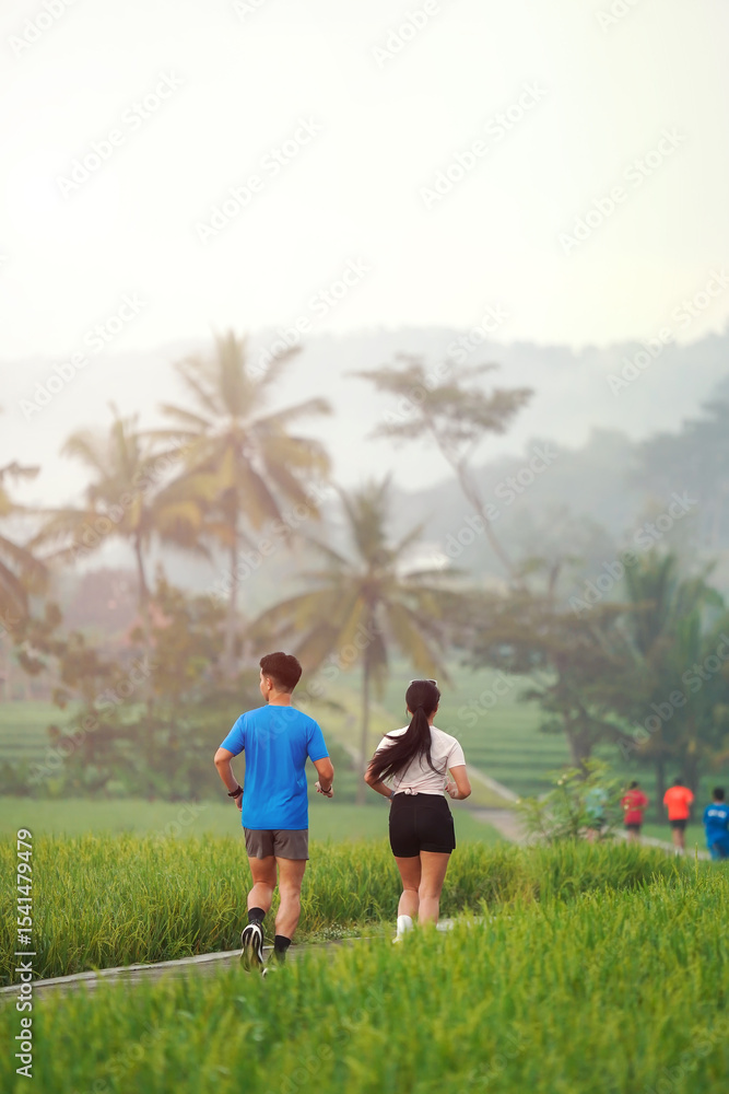 Obraz premium Rear View Asian Couple Jogging Together on Rural Path Surrounded by Green Fields in the Morning