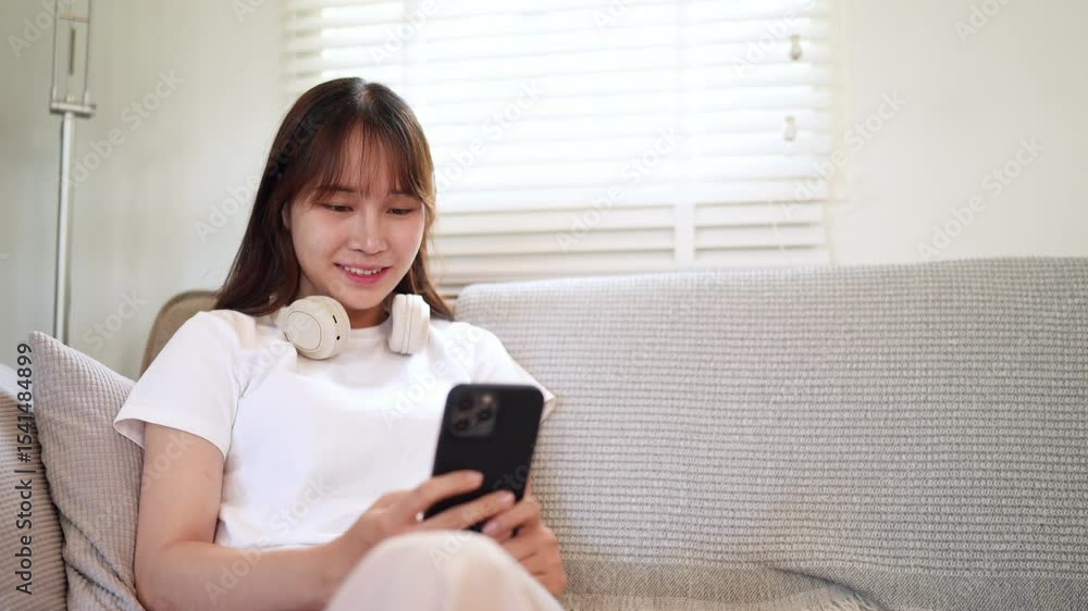 Beautiful Asian woman relaxing on sofa and browsing smartphone at home Beautiful Asian woman relaxing on sofa and browsing smartphone at home