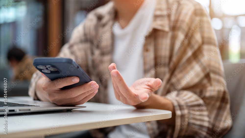 Obraz premium Close up of a man hands holding phone over laptop and talking or explaining sitting at cafe's table.