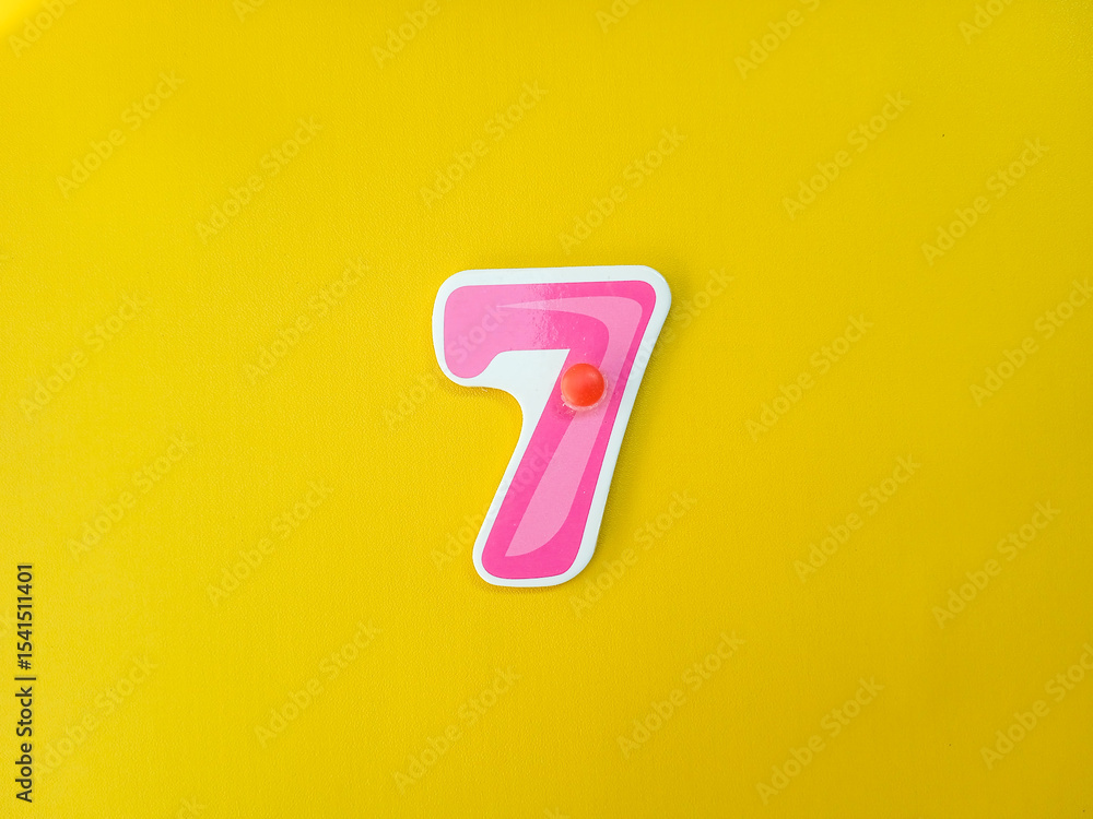 Pink number 7 pinned on yellow background. Close up Pink number 7 pinned on yellow background. Close up