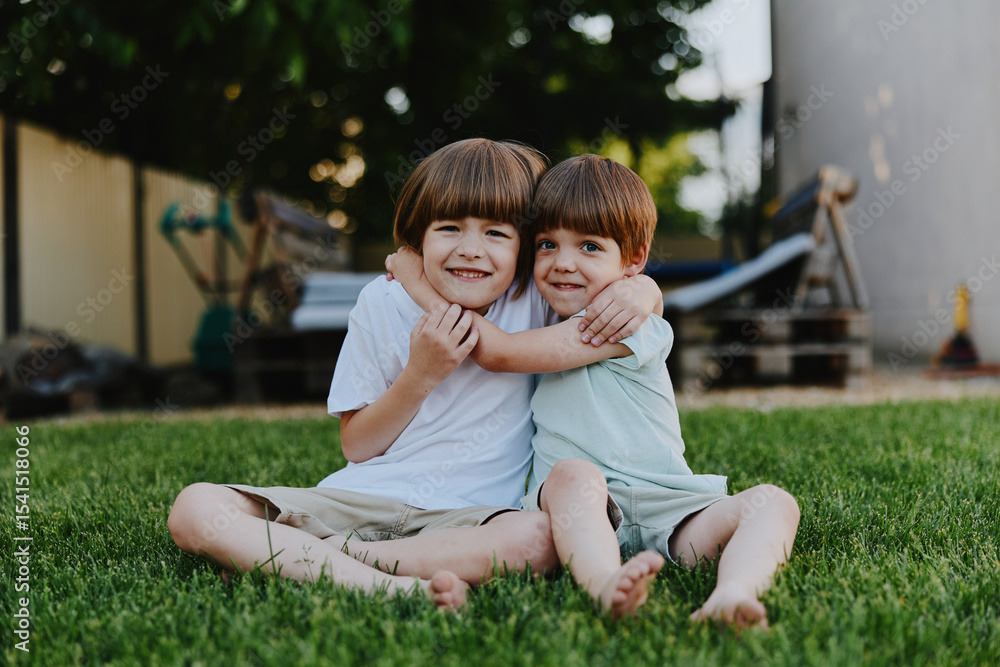 Fototapeta premium Two smiling boys enjoying a sunny day outside, showcasing friendship and joy in a green yard with playful happiness and carefree spirit.