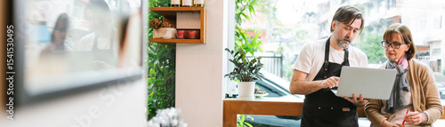Cafe owner and financial advisor discussing business strategy using a laptop in a modern coffee shop. Bright setting with plants and wine bottles, symbolizing collaboration and entrepreneurship.