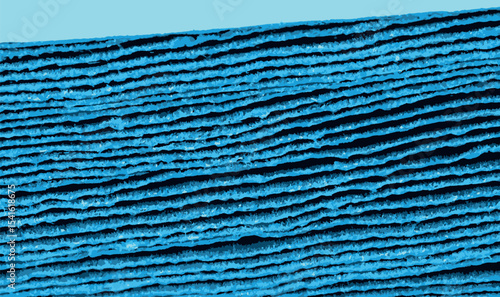 Macro shot of stacked blue corrugated cardboard sheets viewed from the edge, revealing layered texture and intricate linear patterns. Ideal for design, craft, or packaging visuals.