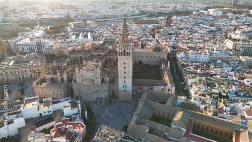 Aerial view of a historic cathedral and surrounding cityscape at sunset, showcasing Gothic architecture and urban layout.