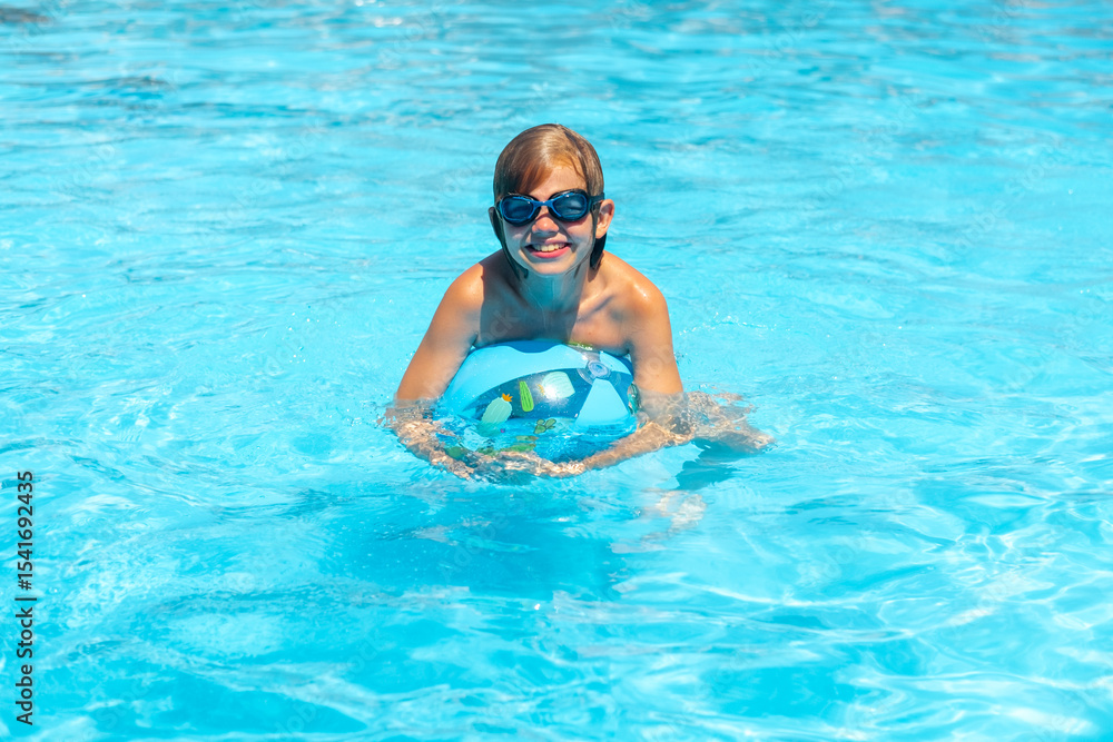 Naklejka premium smiling boy in glasses swimming on Inflatable ball with cheerful face, having fun on Summer travel hotel vacation, Kid relaxing in pool. swimming in blue water. activity, water sport.