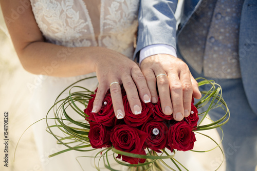 Brautpaar mit Eheringen und Brautstrauß aus roten Rosen – Hochzeitsfoto am Strand