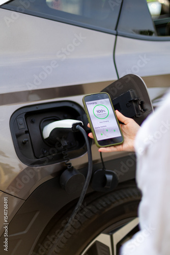 Businesswoman using smartphone app while charging electric car at public station