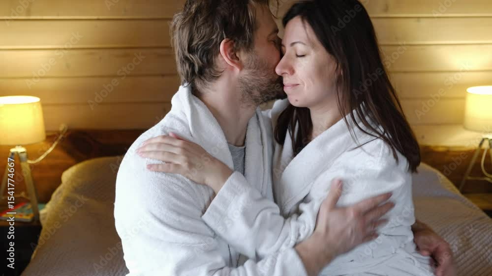 Mature couple in a white bathrobes hugging each other kissing at home bedroom. Intimate Moment. Tender embrace shared between a loving middle age man and woman, husband and wife. Deep love. Vacation Mature couple in a white bathrobes hugging each other kissing at home bedroom. Intimate Moment. Tender embrace shared between a loving middle age man and woman, husband and wife. Deep love. Vacation