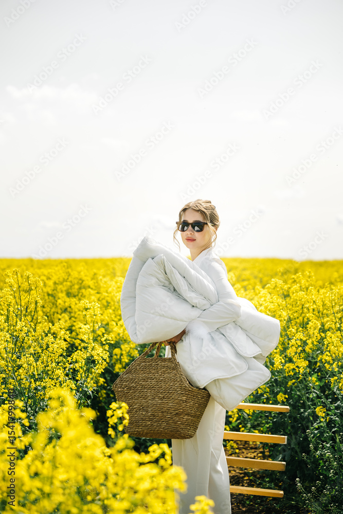 Fototapeta premium Woman carrying a blanket in a bright yellow flower field during a sunny day