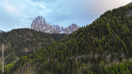 Mountain with snow behind hills with trees, aerial drone photo 4K shot in the Dolomites. Photography for background, postcards, wallpapers.