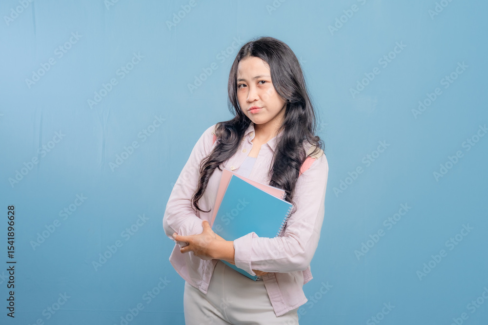 A woman is holding a blue notebook and looking at the camera. She is confused or unsure about something A woman is holding a blue notebook and looking at the camera. She is confused or unsure about something