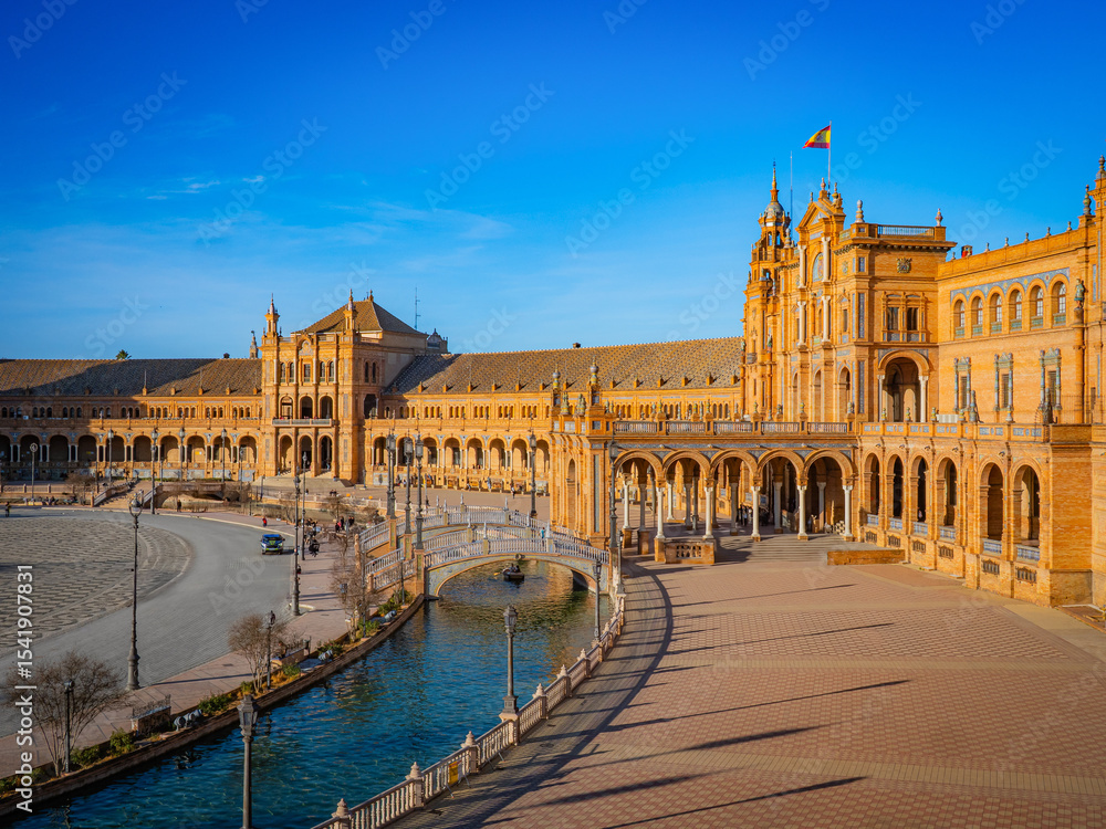 Fototapeta premium Majestic Plaza de España in Seville, Spain, features ornate Renaissance Revival architecture, colorful tiles, and a serene canal under a radiant blue sky.
