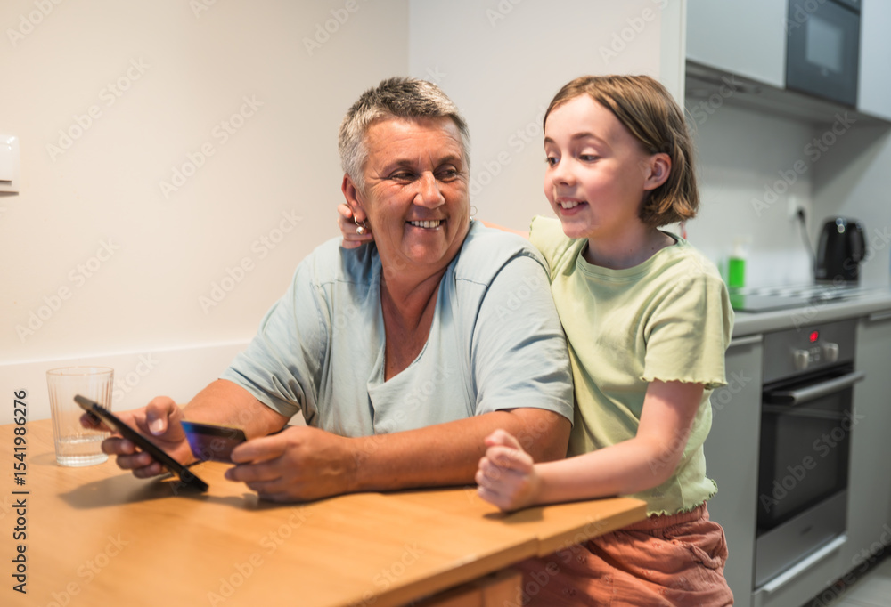 Obraz premium Smiling caucasian grandmother and granddaughter enjoying time together with smartphone. 