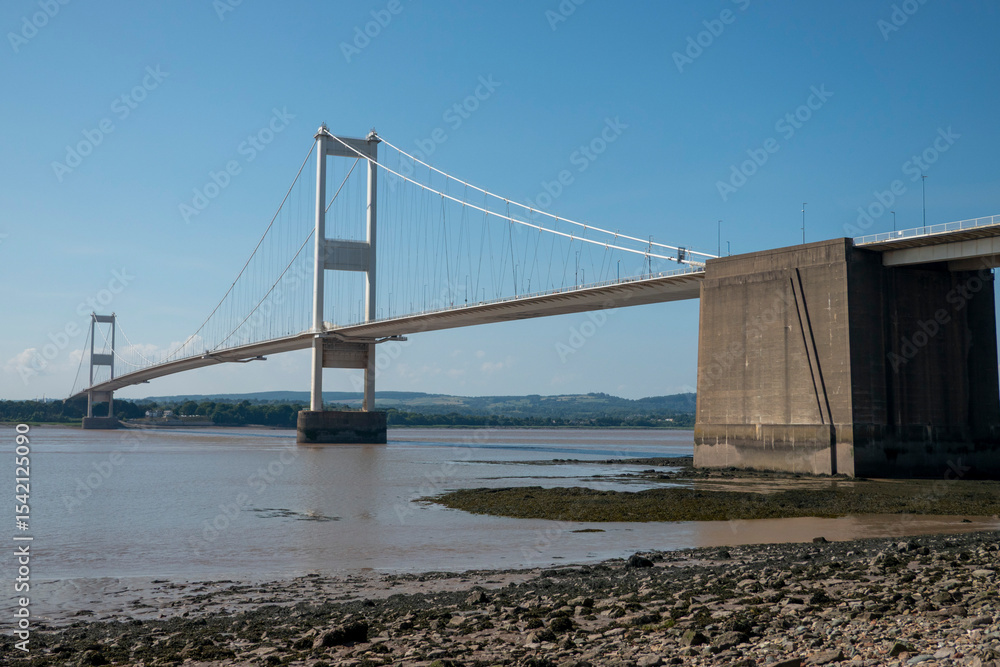 Fototapeta premium The old M48 Severn bridge from England to Wales. Mid with stony shore in foreground