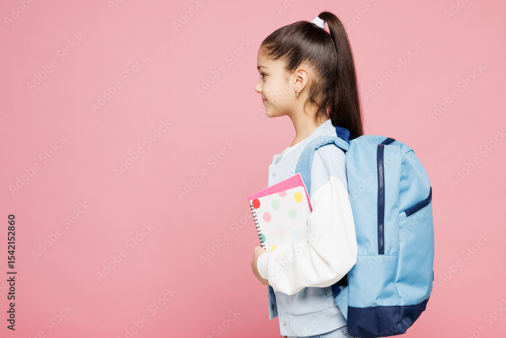 Side profile view young smart school girl 8-9 years old wear blue casual clothes backpack hold books look aside isolated on plain pink background children portrait. Childhood kids education concept. Side profile view young smart school girl 8-9 years old wear blue casual clothes backpack hold books look aside isolated on plain pink background children portrait. Childhood kids education concept.