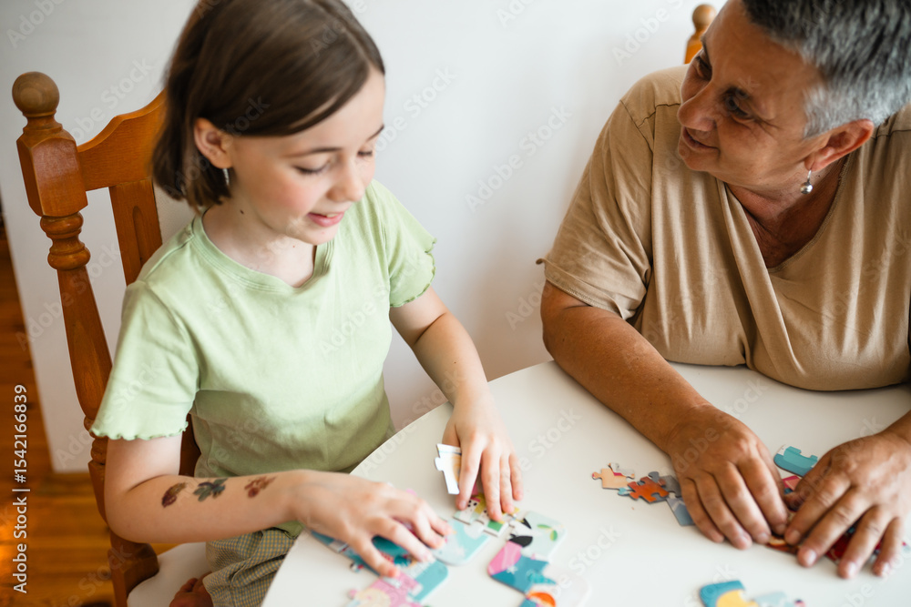 Fototapeta premium Grandmother and granddaughter doing puzzle at home.