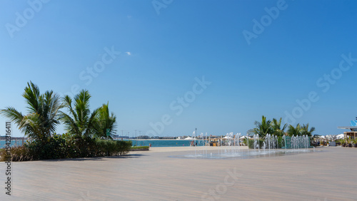 West beach on Palm Jumeirah Island, Dubai on sunny summer day. Fountain on wooden boardwalk. Walking around city