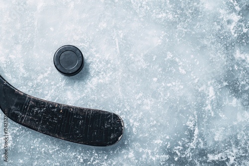 Old black hockey stick and rubber puck resting on ice surface during a quiet moment on the rink