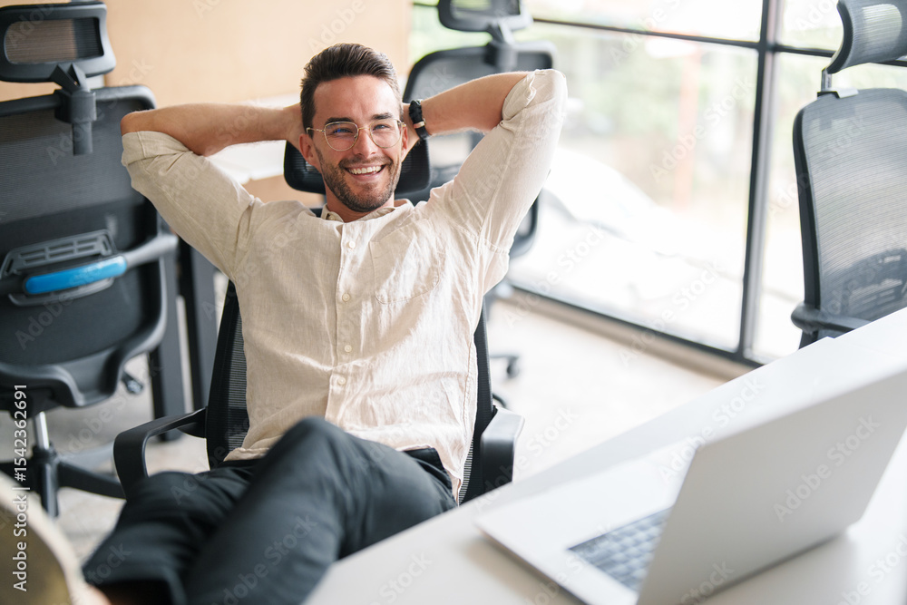 Fototapeta premium Confident Young Man Relaxing in a Bright Modern Office with Minimalist Design and Natural Lighting