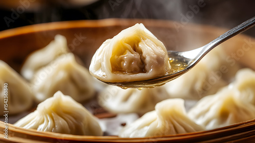 Closeup of freshly steamed xiao long bao soup dumplings in bamboo steamer, with one dumpling on spoon