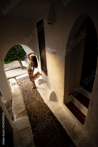 oung girl in pants leans pose against a white wall in the sunset sunlight of the fishing village of Binibeca