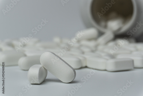 White pills tablets spilled from a bottle on a light grey background 