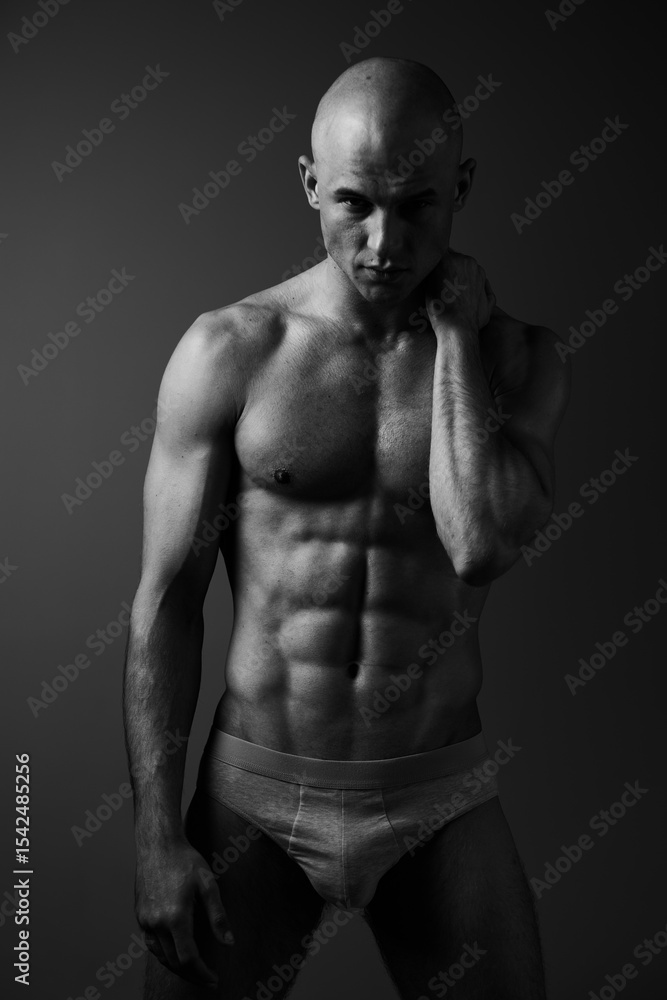 Fototapeta premium Black and white portrait of a muscular man conveying strength and confidence, showcasing his sculpted physique in dramatic lighting.