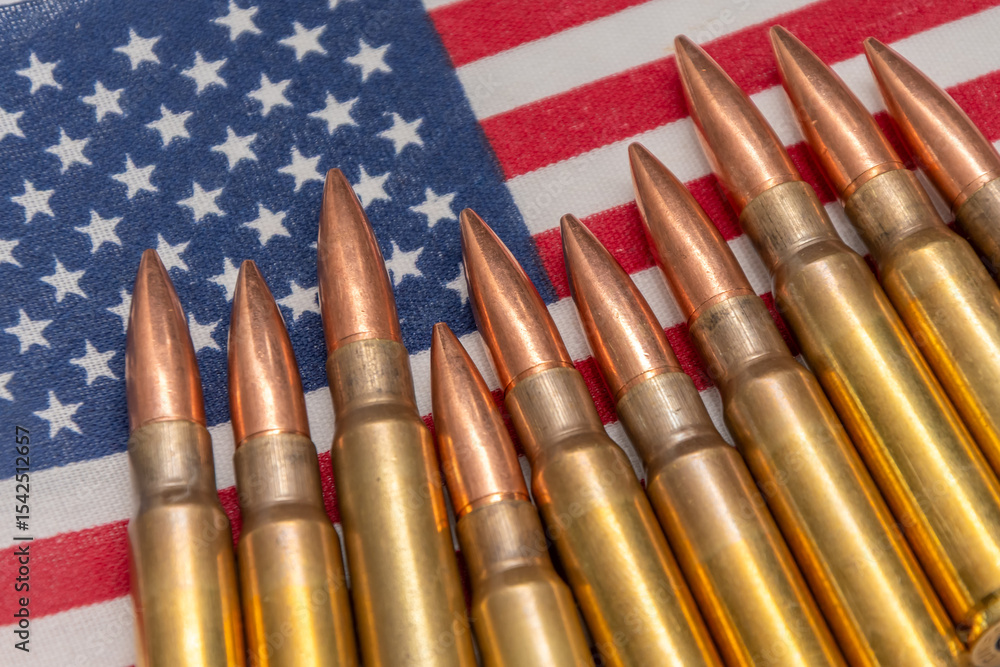 Obraz premium Firearms cartridges arranged in a row on the background of the American flag. The image symbolises guns, patriotism, the right to self-defence and military themes in the USA.