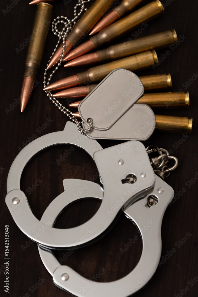 Naklejka premium Symbolic combination of handcuffs, tokens and bullets on a dark wooden background. Suitable for illustrating the concepts of war, peace, crime, punishment and defence.
