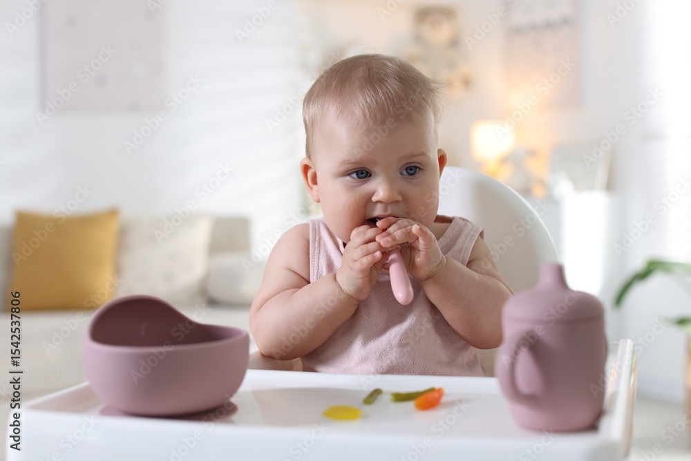 Cute little baby eating with spoon on feeding chair at home Cute little baby eating with spoon on feeding chair at home