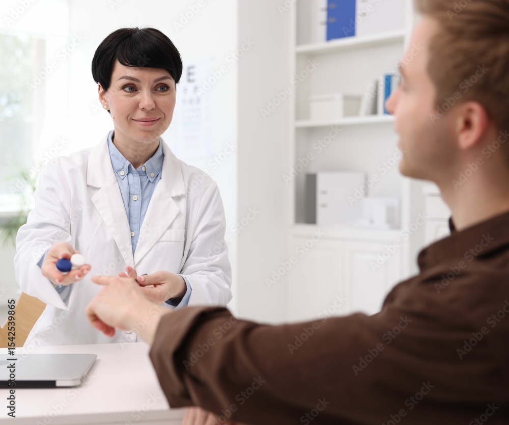 Fototapeta premium Ophthalmologist giving contact lenses to patient at white table in clinic